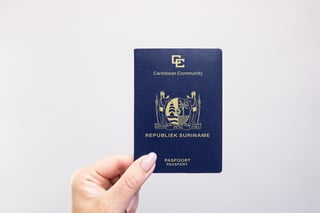 Gros plan d'un passeport du Suriname tenu à la main sur fond blanc uni
