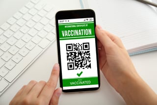 woman holding smartphone with international certificate of vaccination at white table