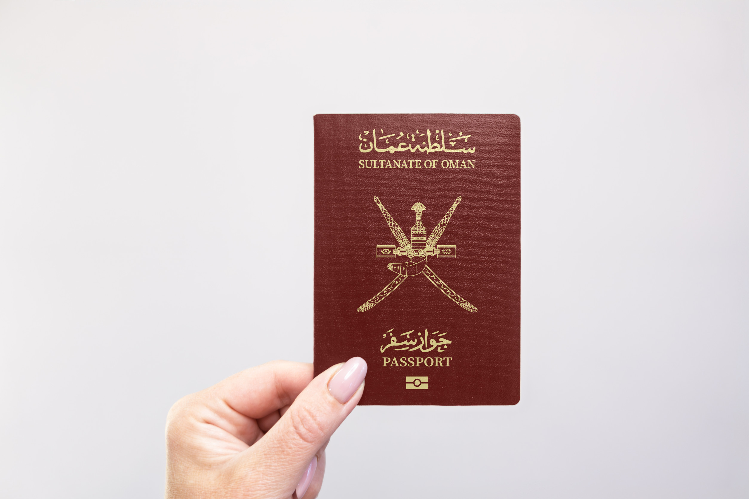 Nahaufnahme eines omanischen Reisepasses, der in der Hand vor weißem Hintergrund gehalten wird