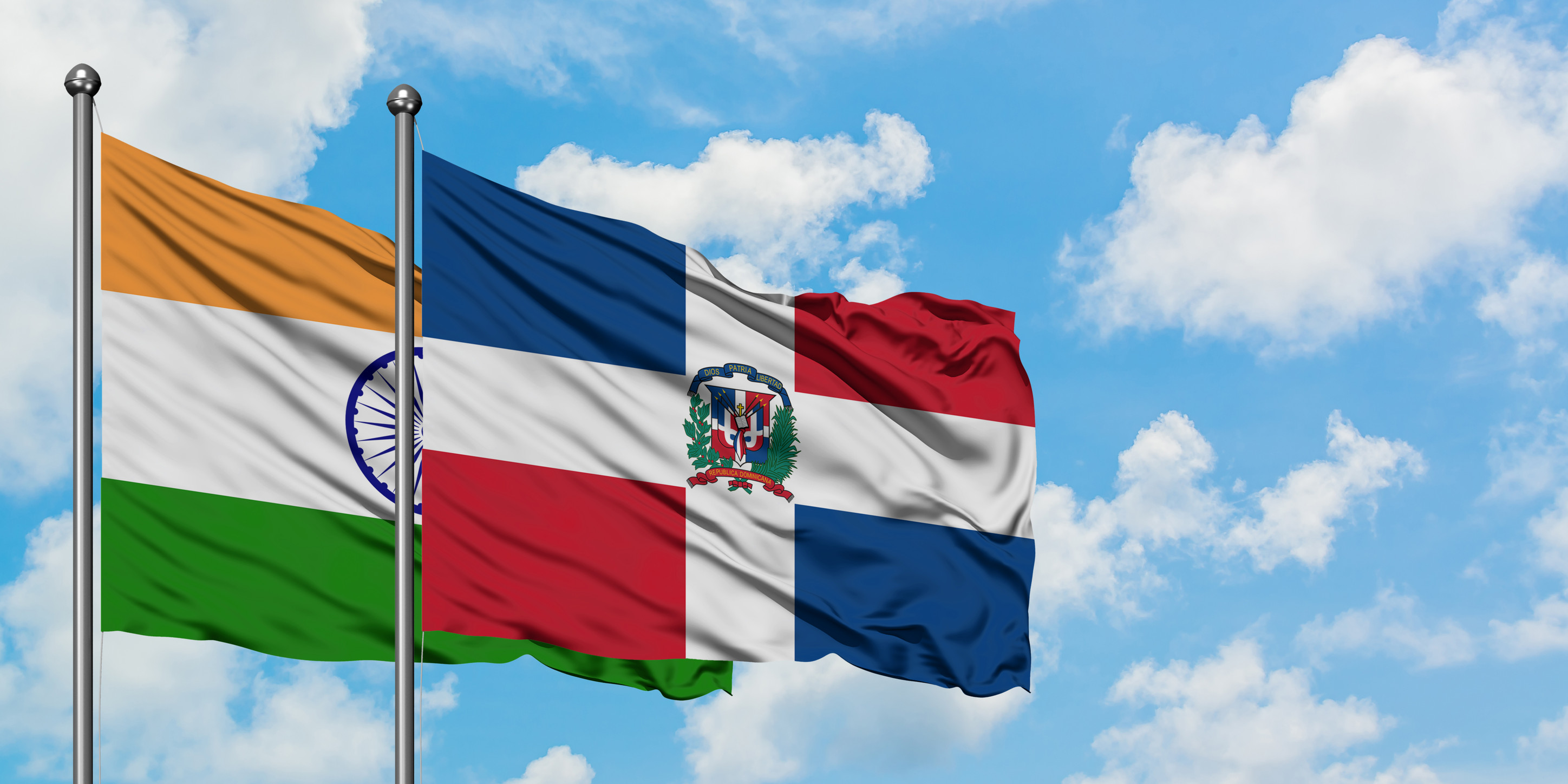 Indische und Dominikanische Republik Flaggen wehen im Wind vor blauem Himmel mit weißen Wolken