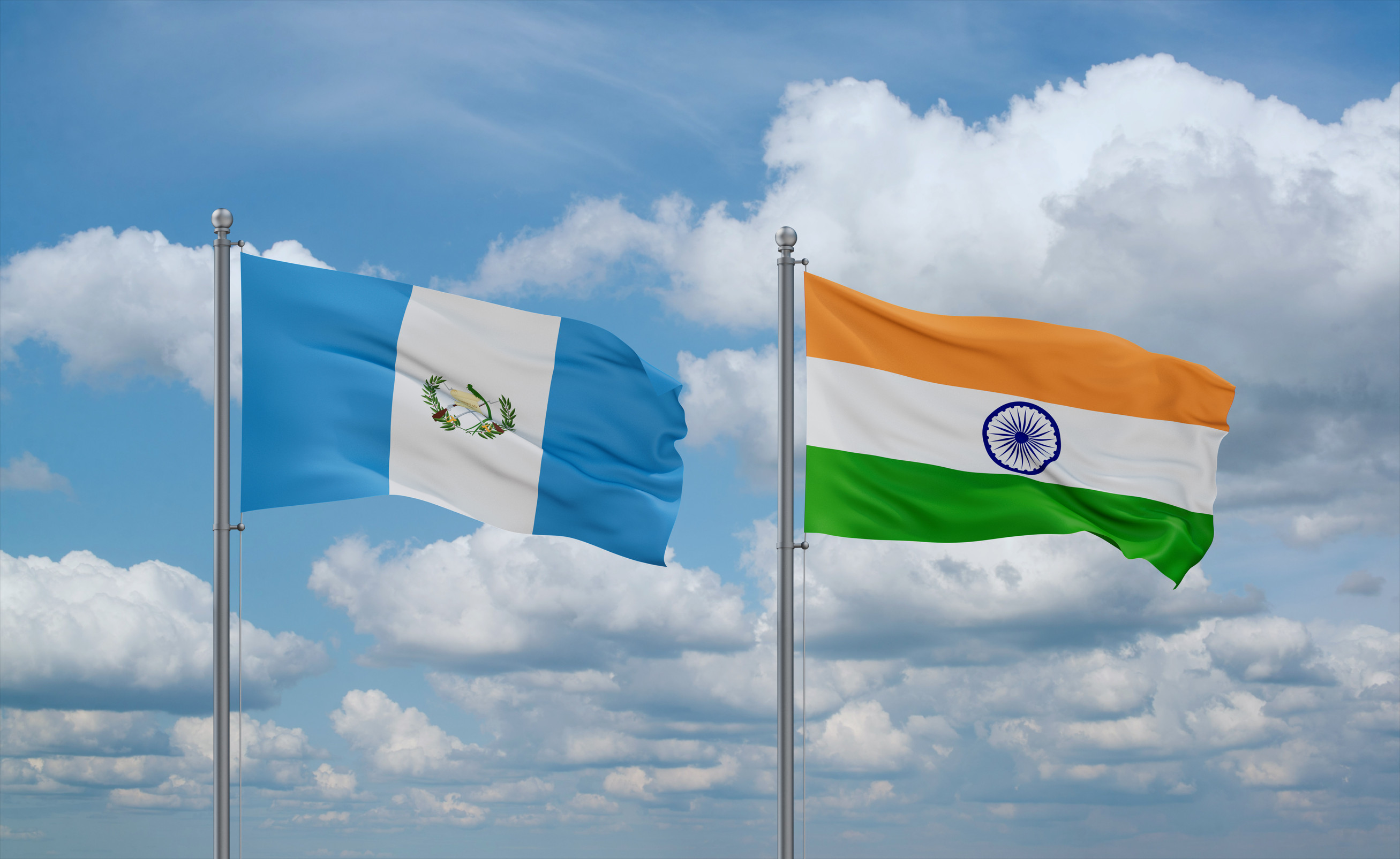 Indische und guatemaltekische Flaggen wehen gemeinsam am blauen, wolkigen Himmel – Beziehung zwischen zwei Ländern
