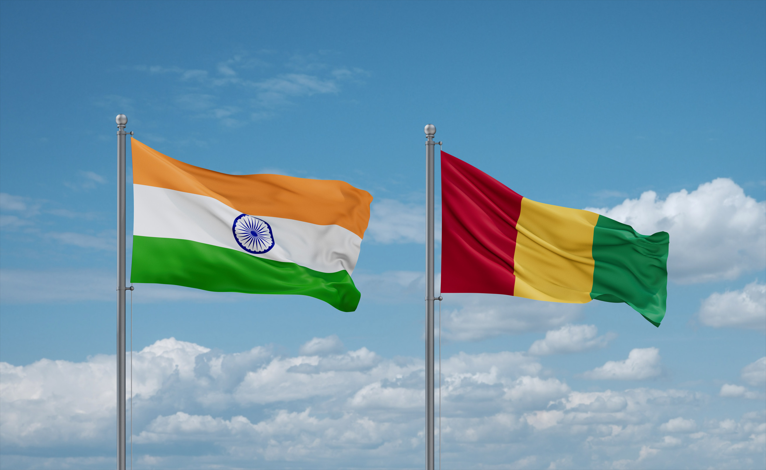 Nahaufnahme der wehenden Flaggen von Guinea und Indien vor blauem, wolkigem Himmel