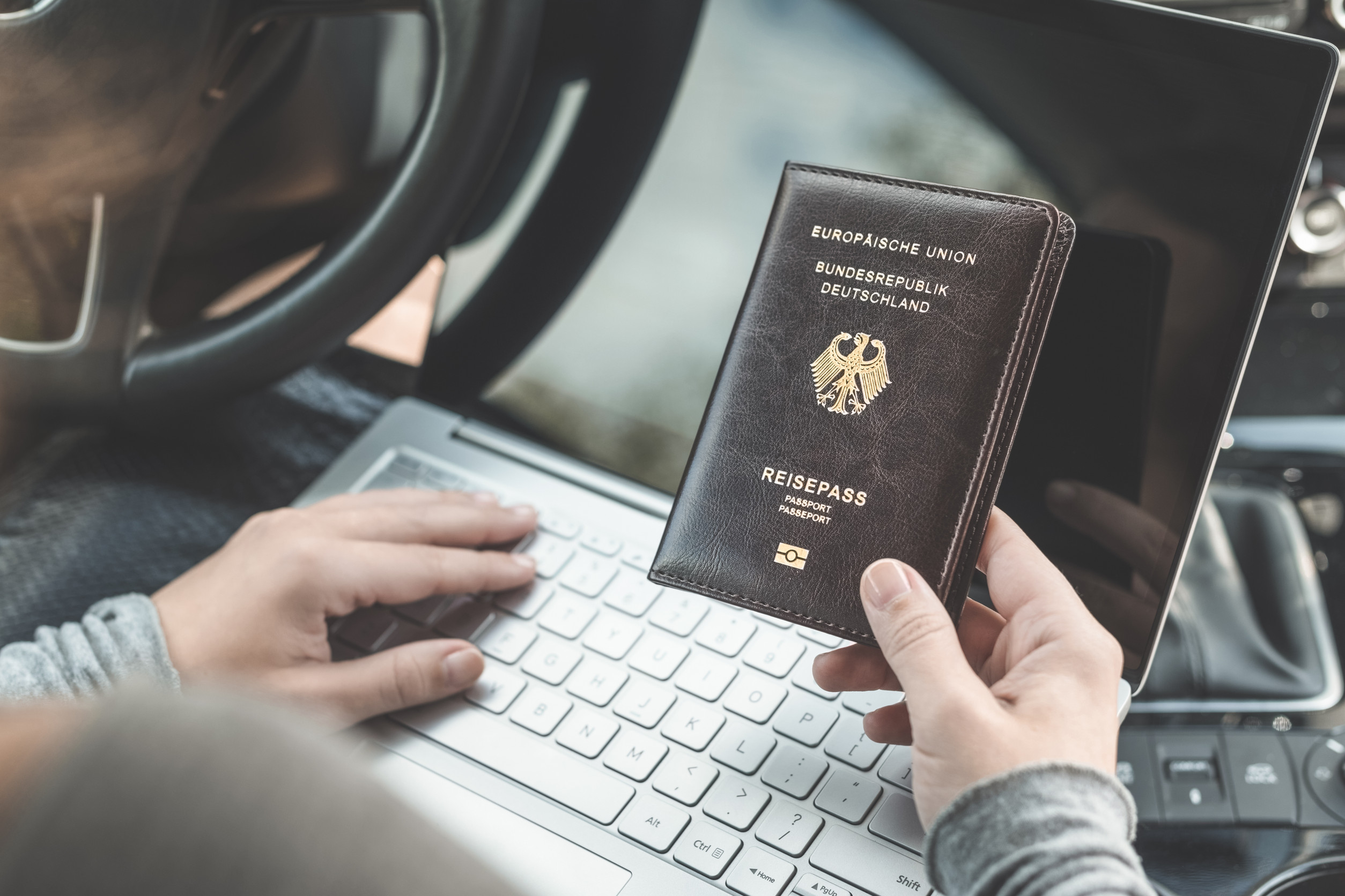 Frau im Auto mit Laptop und deutschem Reisepass – Reisekonzept